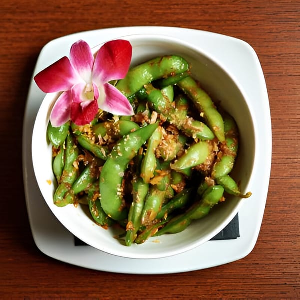 A white bowl of edamame with garlic and sesame seeds, garnished with a pink orchid.
