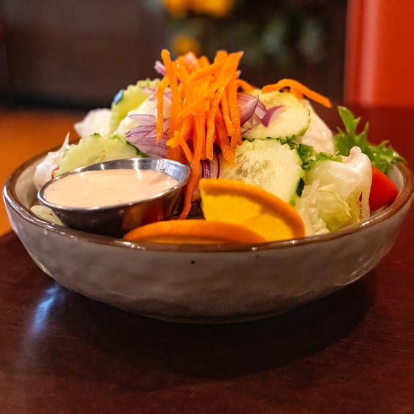 Fresh salad with shredded carrots, cucumber, red onion, and orange slices, with a side of dressing.